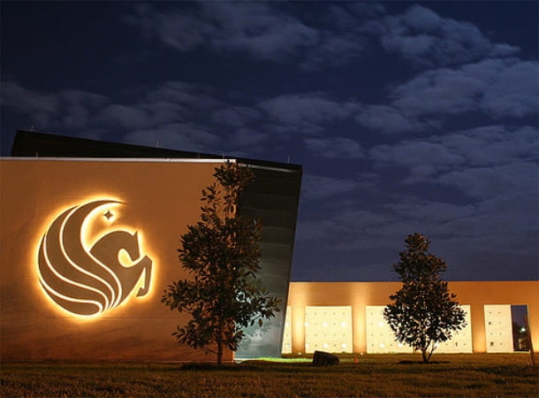 The UCF logo illuminated on a campus building at night
